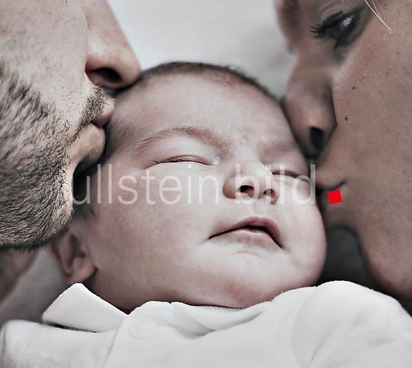 Father and mother lovingly kissing their baby