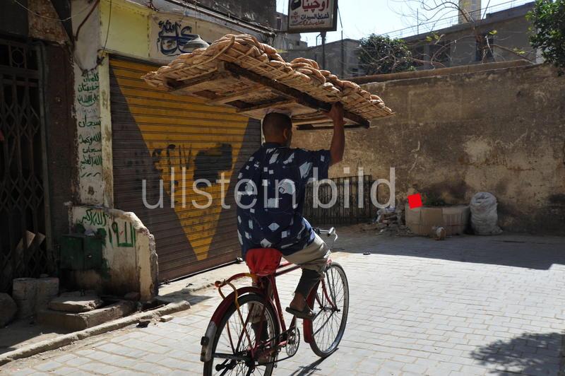 Kairo Straßenszene im ehemaligen jüdischen Viertel Haret al-Yahoud. Ein Baecker liefert frische Fladenbrote mit dem Fahrrad aus